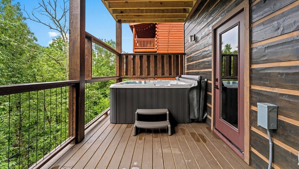 A wooden deck with a hot tub, a small table, and a bench. - Luxury Cabin w/Pool, Hot Tub, Game Room, Bar, Movie Room & Mountain Views (Sevierville)