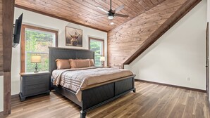 A bedroom with a sloped ceiling, a bed with a dark headboard, two bedside tables, a lamp, and a ceiling fan. - Luxury Cabin w/Pool, Hot Tub, Game Room, Bar, Movie Room & Mountain Views (Sevierville)