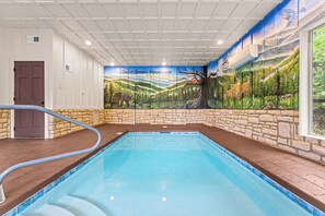 An indoor swimming pool with a mural of Great Smoky Mountains wildlife, stone walls, and a door. - The Ridgeline Reserve • Luxe Lodge w/ Private Indoor Pool • Top 5% (Sevierville)