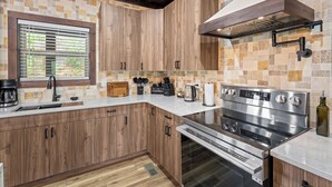 A modern kitchen with wooden cabinets, a stainless steel stove, and a window with blinds. - Luxury Cabin w/Pool, Hot Tub, Game Room, Bar, Movie Room & Mountain Views (Sevierville)