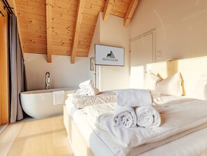 Ein Hotelzimmer mit einem Bett, einer Badewanne und einem an der Wand befestigten Fernseher, der 'REHFUGIUM' zeigt.