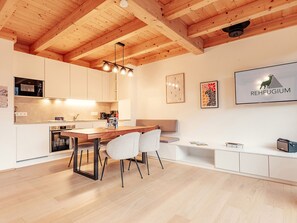 Eine moderne Küche mit Holzbalken, ein Essbereich mit Tisch und Stühlen sowie ein weißes Sofa.
