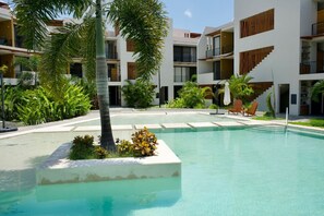 A modern hotel with a central swimming pool, surrounded by lush greenery and multiple balconies. - Modern Condo in Flamingos - Pool Gym Concierge (Bucerías)