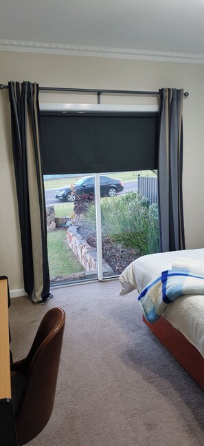 A hotel room with a bed, a chair, a window with curtains, and a view of a street and greenery outside.