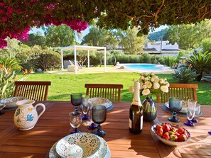A wooden table set for a meal with a view of a pool and garden. - Villa Carlebia - Private pool and garden. Beaches within walking distance, ideal for families (Sinnai)