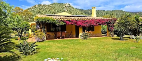 Une maison avec un jardin, une terrasse avec des chaises et une montagne en arrière-plan.