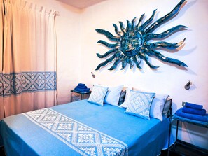 A bedroom with a bed, a wall-mounted sun decoration, a side table with towels, and a curtain. - Villa Carlebia - Private pool and garden. Beaches within walking distance, ideal for families (Sinnai)