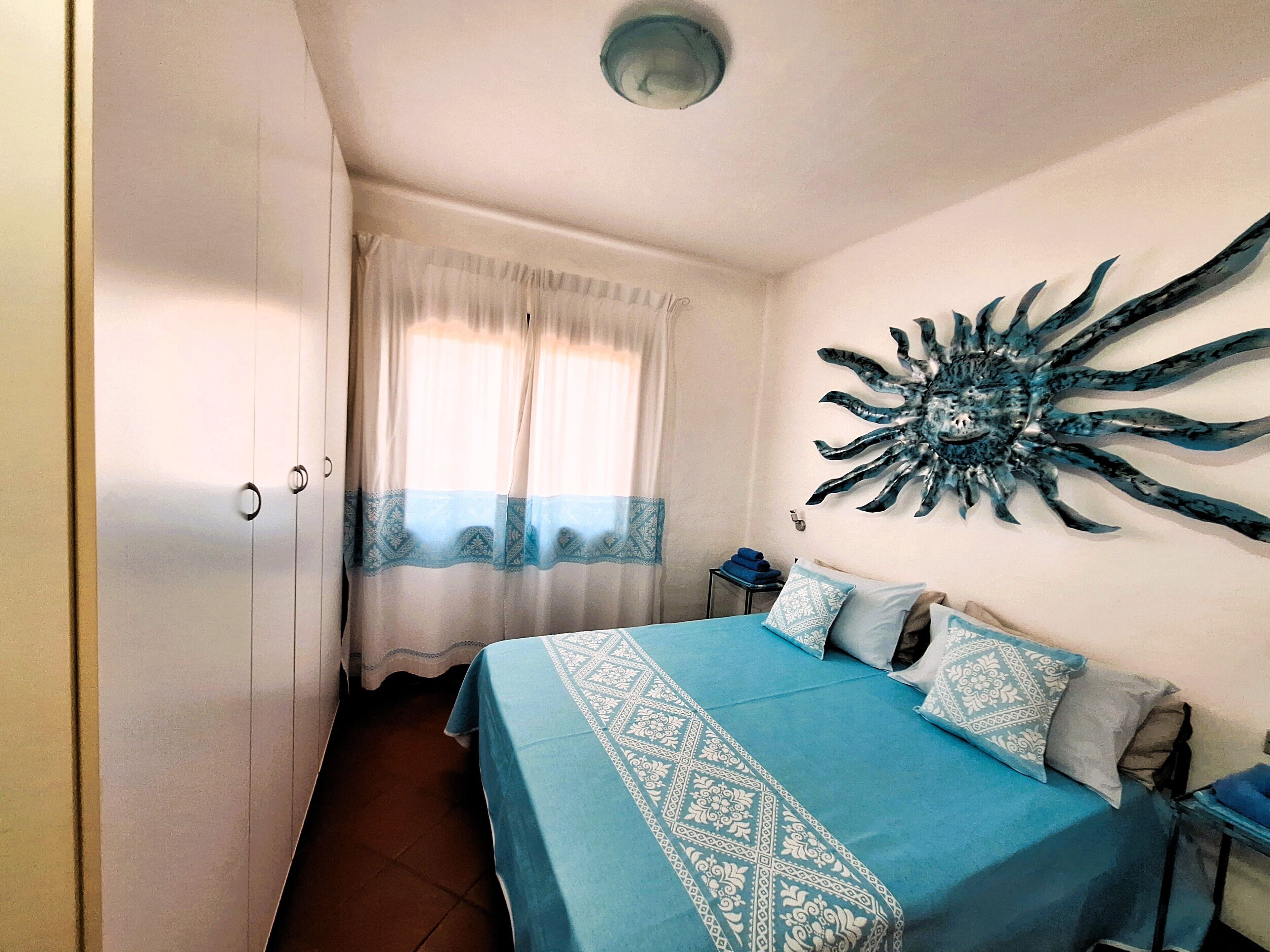 A bedroom with a bed, curtains, a wall decoration, and a nightstand.