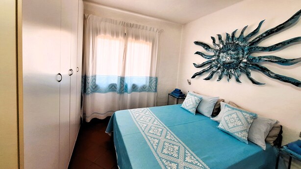 A bedroom with a bed, curtains, a wall decoration, and a nightstand. - Villa Carlebia - Private pool and garden. Beaches within walking distance, ideal for families (Sinnai)