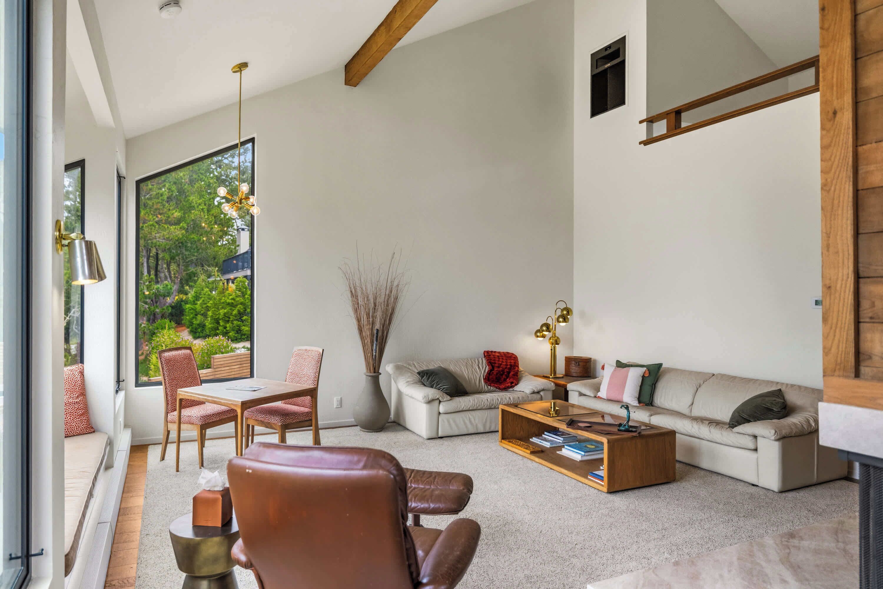 Un salon moderne avec un canapé, une table basse et des fauteuils, de grandes fenêtres et une vue sur la verdure.