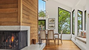Ein modernes Interieur mit Kamin, Essbereich und großen Fenstern mit Blick auf Grünflächen.