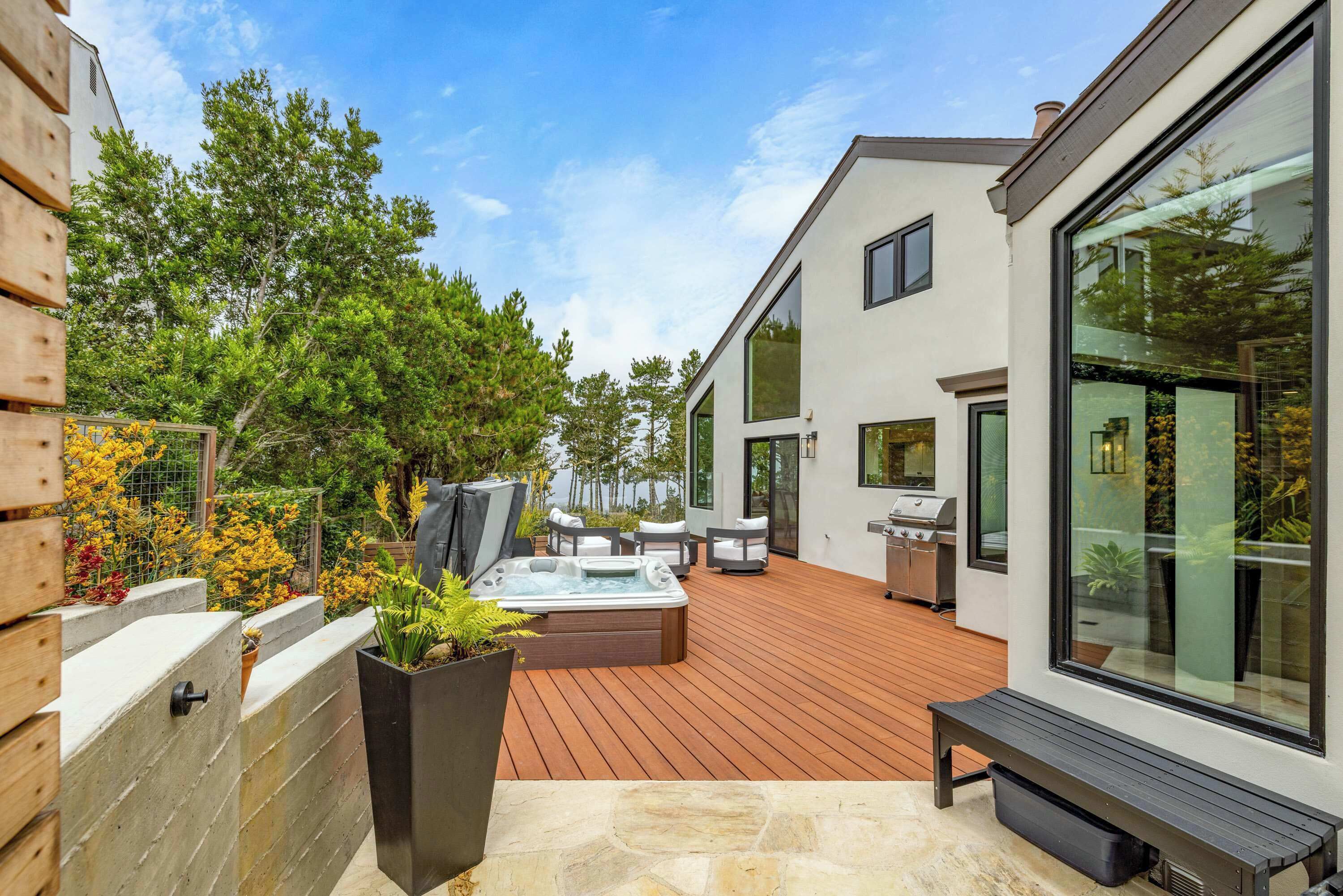 A modern outdoor patio with a hot tub, seating, and a barbecue area.