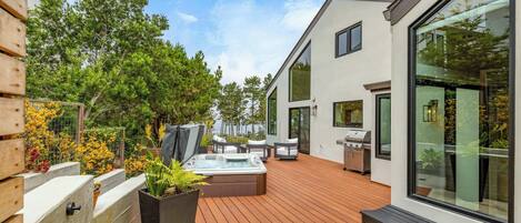 A modern outdoor patio with a hot tub, seating, and a barbecue area.