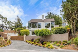 Une maison moderne à deux étages, avec une allée menant à une entrée fermée par un portail.