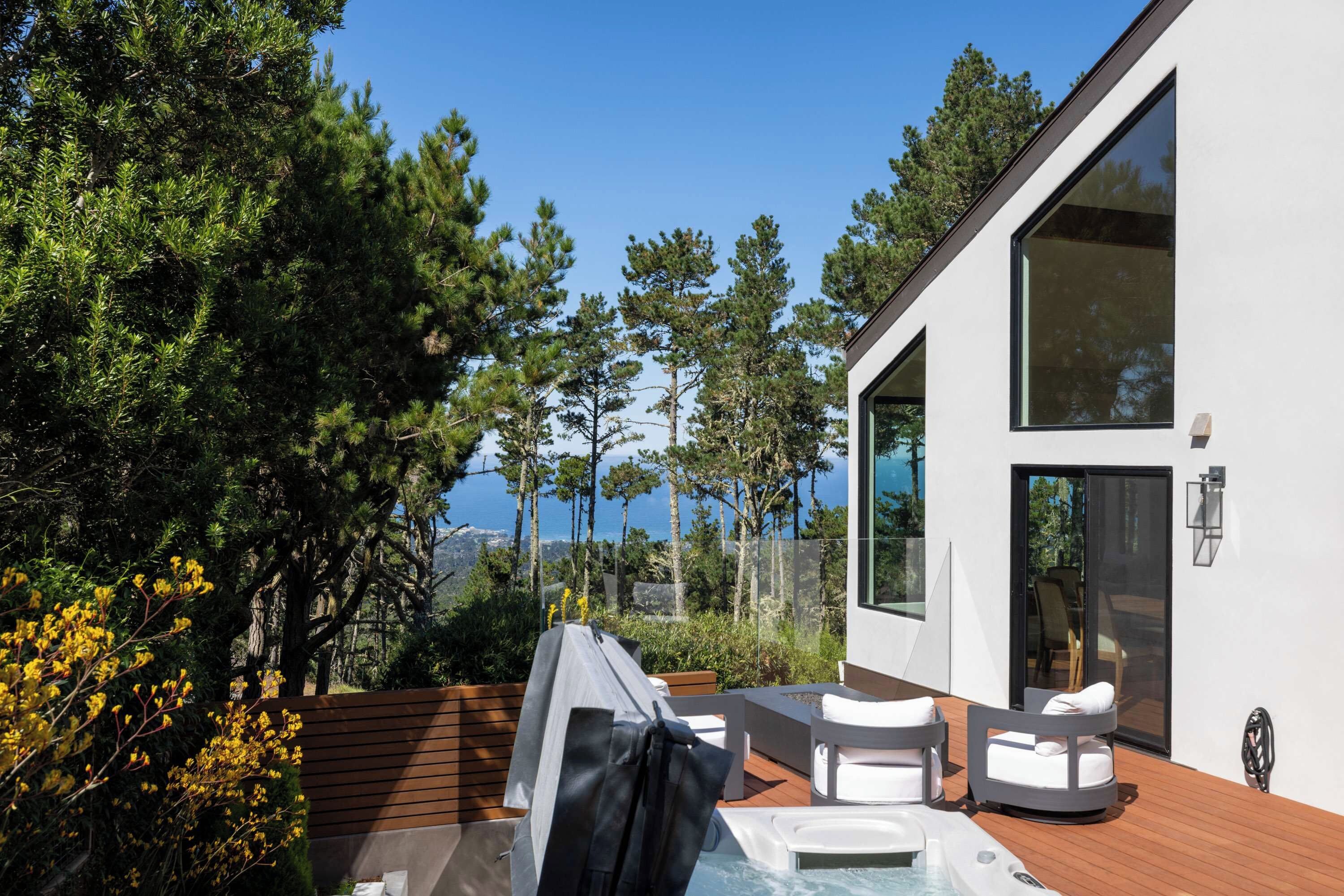 Ein moderner Außenbereich mit Whirlpool, mit Blick auf eine bewaldete Landschaft und ein Gewässer.