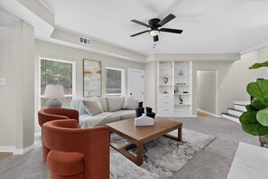 A modern living room with a sofa, coffee table, and chairs, a ceiling fan, and a bookshelf. - Cozy 2-bedroom house in tranquil Greenville with AC (Greenville)