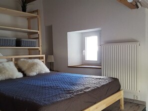 Ein Schlafzimmer mit einem Bett, einem Fenster, einer Heizung und Regalen mit Körben.