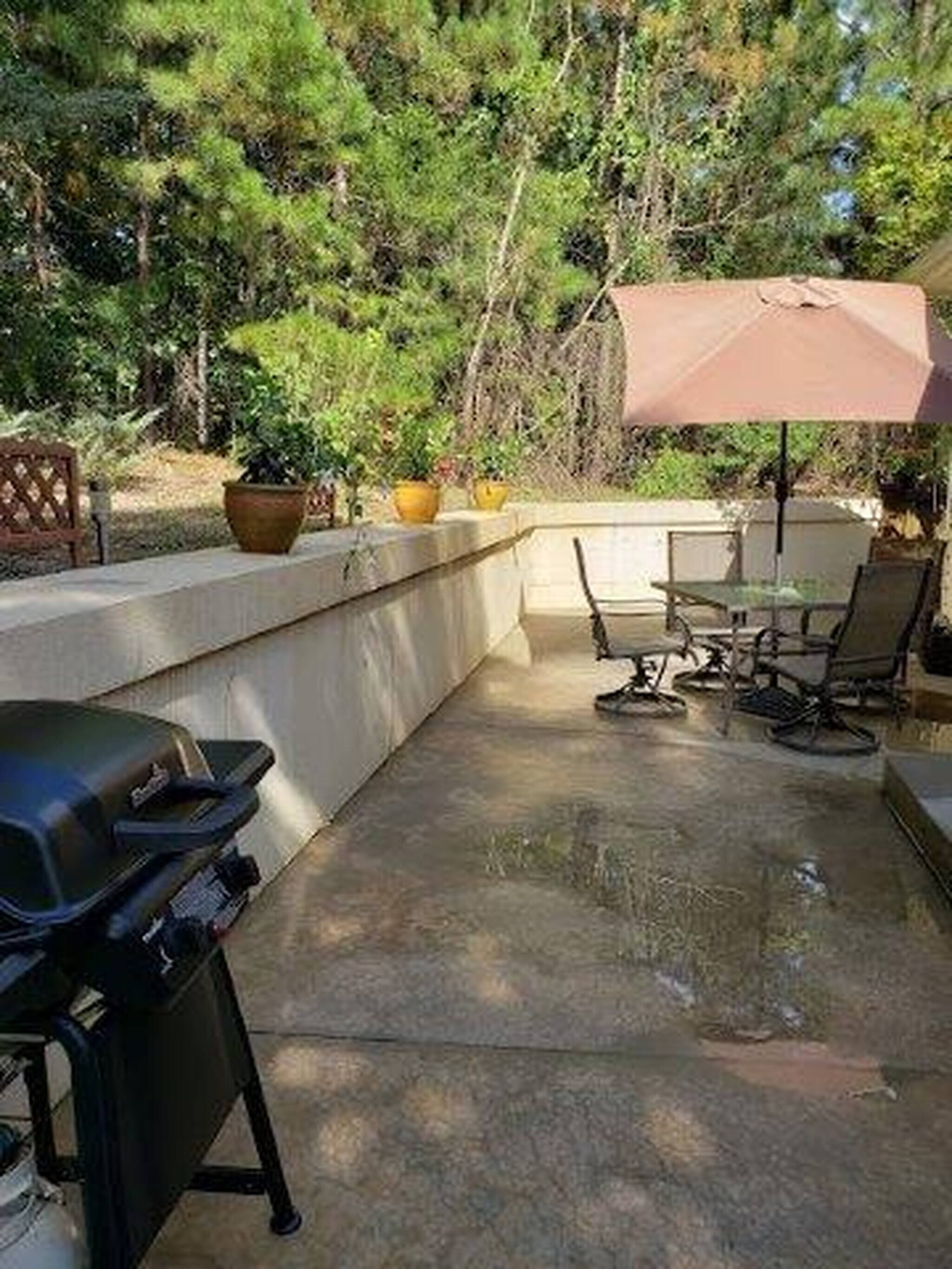 An outdoor patio with a grill, seating, and potted plants.