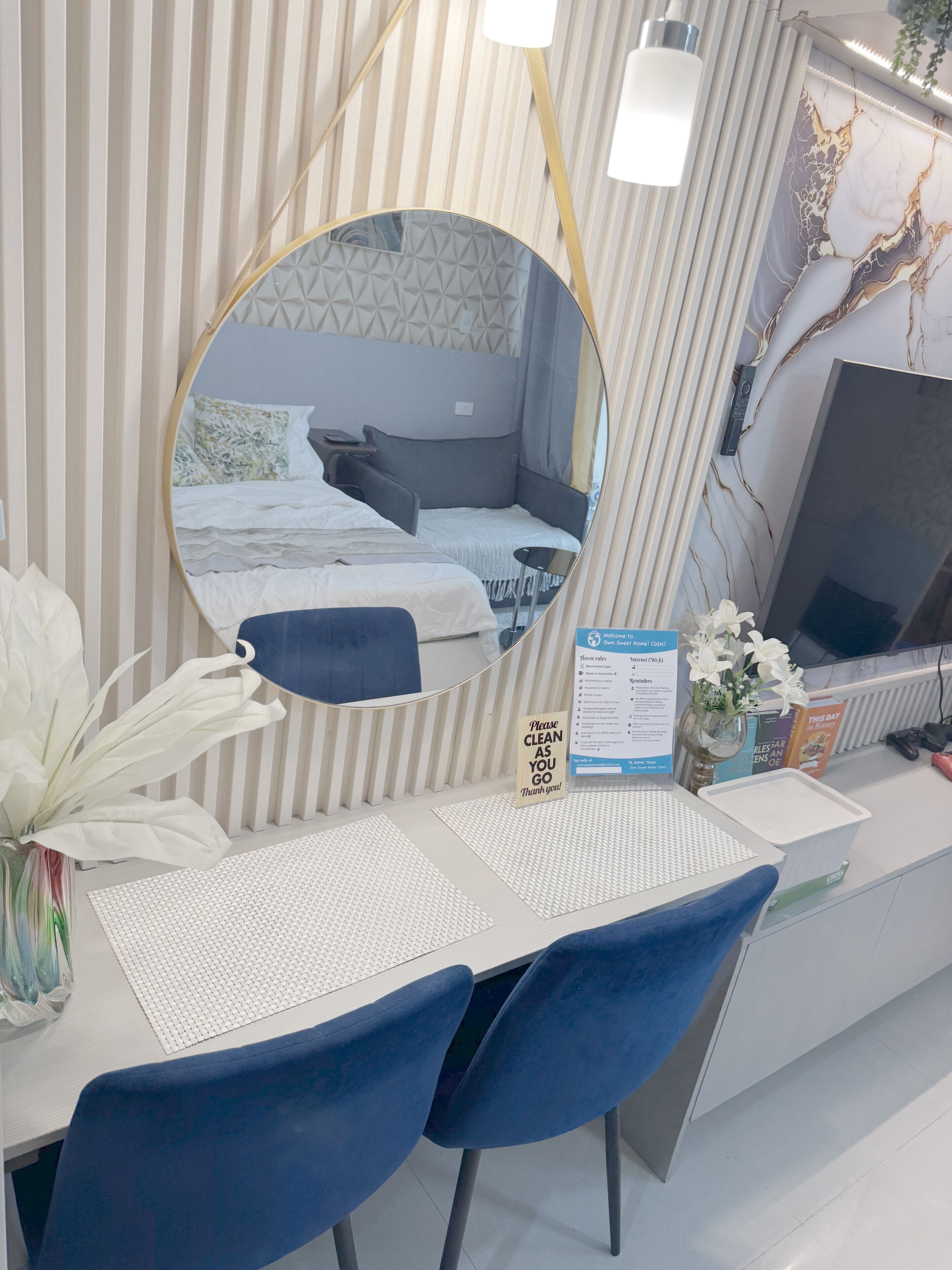 Une chambre d’hôtel avec un lit, un bureau et une chaise, un miroir, un vase avec des fleurs et un panneau.