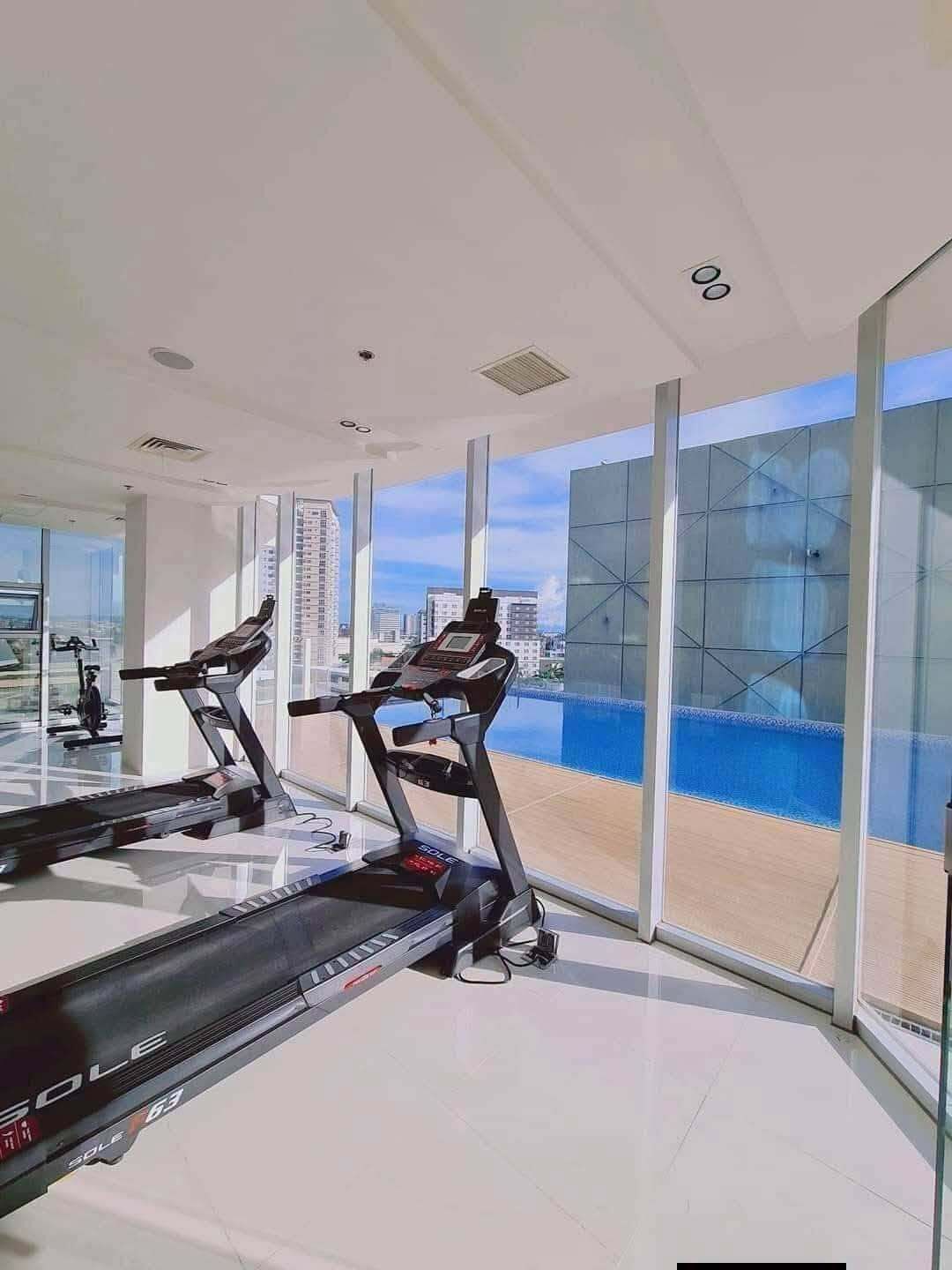 Ein Fitnessstudio mit Laufbändern und Blick auf die Stadt durch große Fenster.