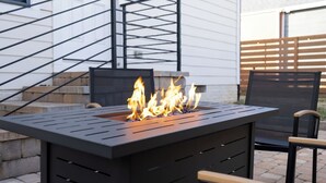 A black outdoor fire feature with flames, a black metal chair, and a wooden bench. - The Mulberry at 121 Lincoln (Raleigh)