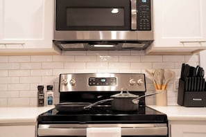 A kitchen with a microwave, oven, and stove. There are spices and utensils on the counter. - The Mulberry at 121 Lincoln (Raleigh)