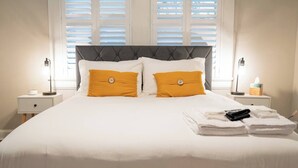 A neatly made bed with white bedding and two orange pillows, flanked by bedside tables with lamps and a tissue box. - The Mulberry at 121 Lincoln (Raleigh)