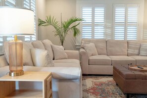 A living room with a sofa, ottoman, lamp, and a plant. - The Mulberry at 121 Lincoln (Raleigh)