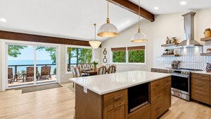 A modern kitchen with a large island, wooden cabinets, stainless steel appliances, and a view to the outside. - Drift + Dune | Indoor Pool on Lake Michigan (Two Rivers)