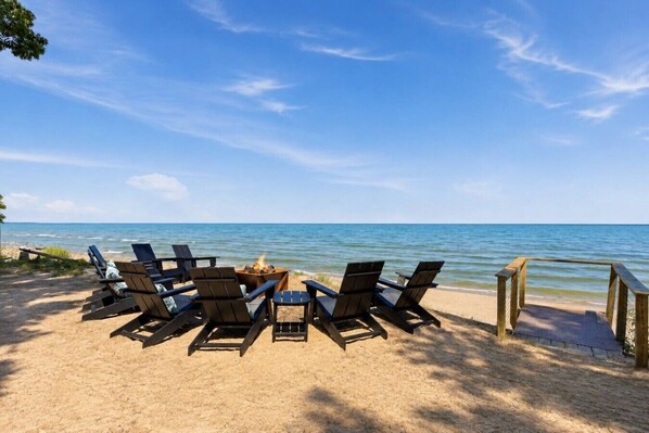 A beachside seating area with a fire pit and chairs facing the ocean.