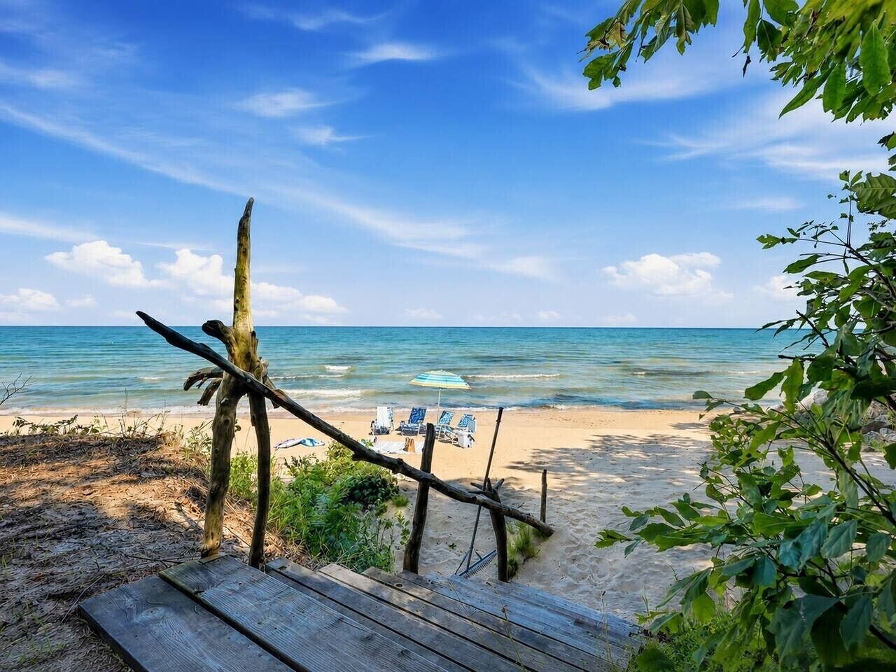 A wooden deck leading to a beach with lounge chairs and an umbrella.