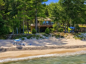 A beachfront property with a large house, a sandy beach, and a small pool area.