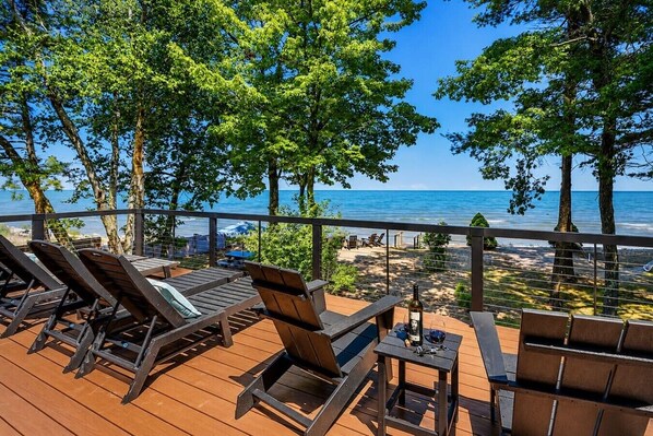A wooden deck with lounge chairs and a table, overlooking a beach and ocean.