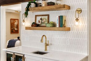 A kitchen with a white countertop, a gold faucet, and two wooden shelves with decorative items.