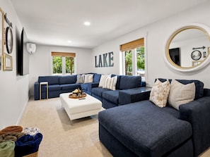Un salon moderne avec un canapé d’angle, un pouf blanc et un grand miroir.
