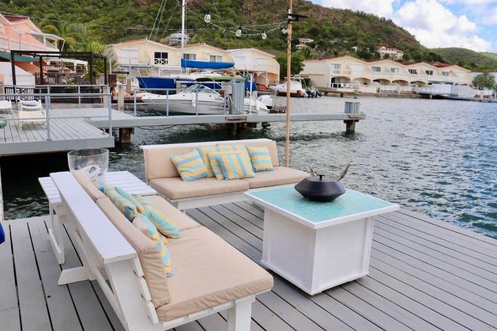 A deck with lounge chairs and a table, overlooking a marina with boats and buildings.