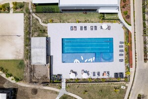 Vue aérienne d’un espace piscine comprenant une piscine rectangulaire, des allées qui l’entourent et quelques chaises longues.