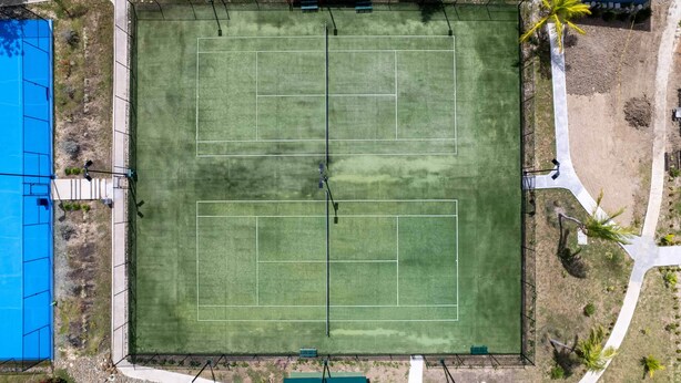 Een tennisbaan met omliggende paden en een blauwe constructie.