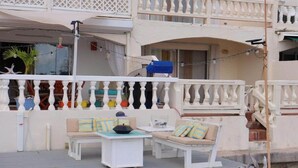 Een balkon met witte hekwerkjes, een witte tafel en een beige bank met gestreepte kussens.