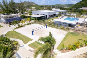 A sports court with a volleyball net, surrounded by a landscaped area with palm trees and a pool. - La Dolce Villa in Jolly Harbour Antigua (Jolly Harbour)