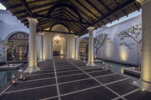 A spacious indoor area with a pool, columns, and a covered walkway.