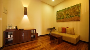 Una habitación con piso de madera, un sofá, un aparador, un cuadro y una lámpara.