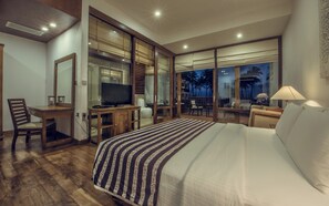 Habitación de hotel con una cama grande, un escritorio con televisor, una silla y vistas a palmeras a través de la ventana.