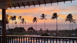 Un balcón con vista al océano y palmeras al atardecer.