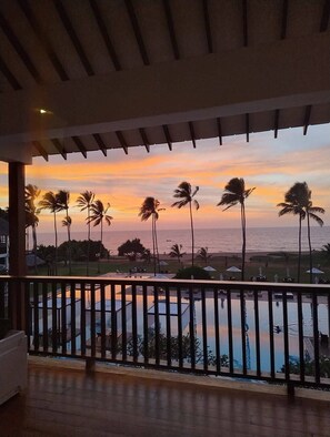 A balcony with a view of the ocean and palm trees during sunset.