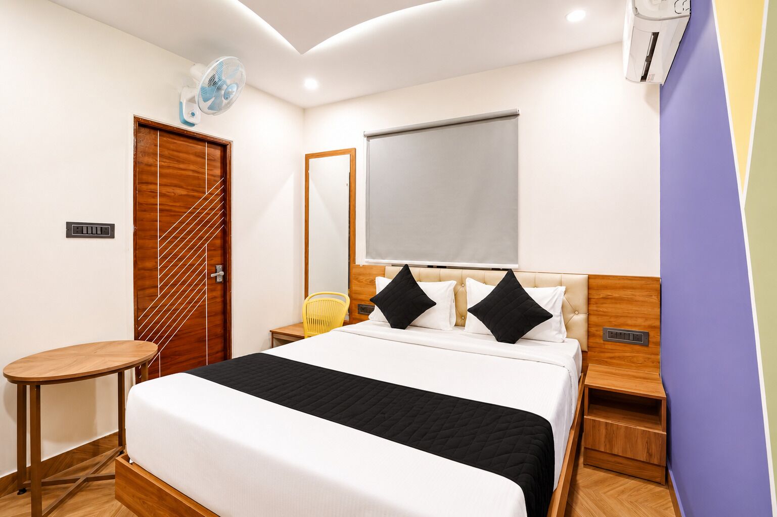 Una habitación de hotel con cama, mesitas de noche, una silla, escritorio y equipo de aire acondicionado.