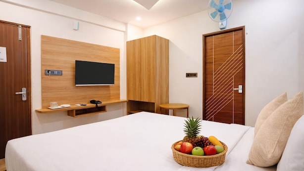 Una habitación de hotel moderna con una cama grande, un televisor montado en la pared, un armario de madera, una mesita y una cesta de frutas sobre la cama.