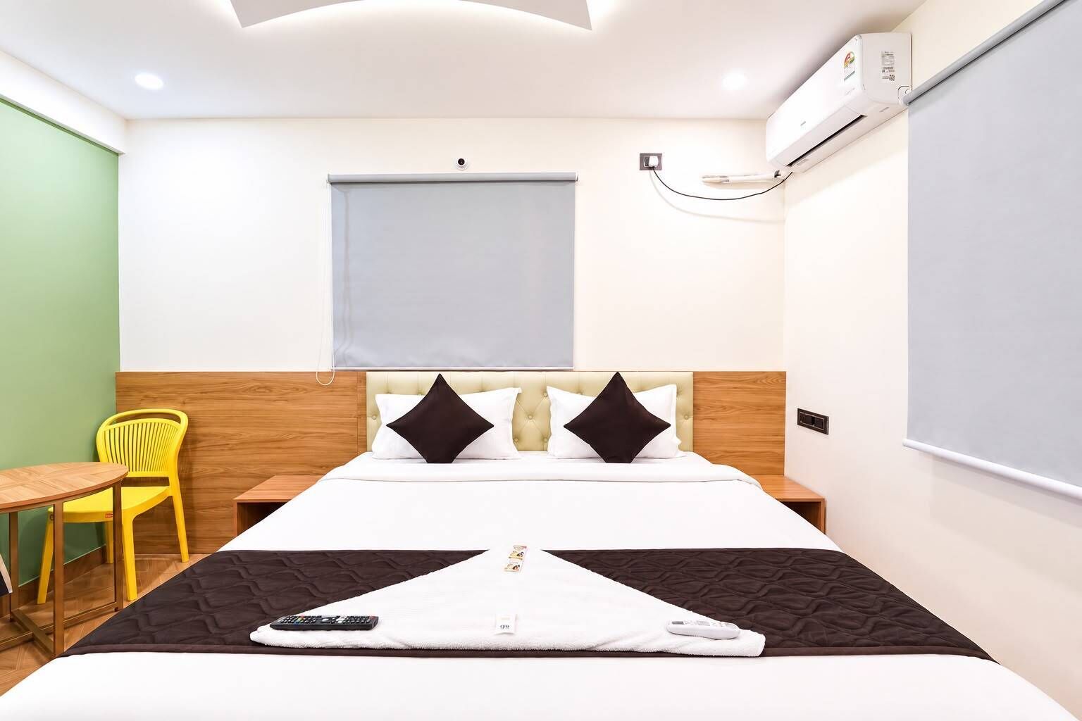 A hotel room with a bed, a desk, a chair, and an air conditioning unit.