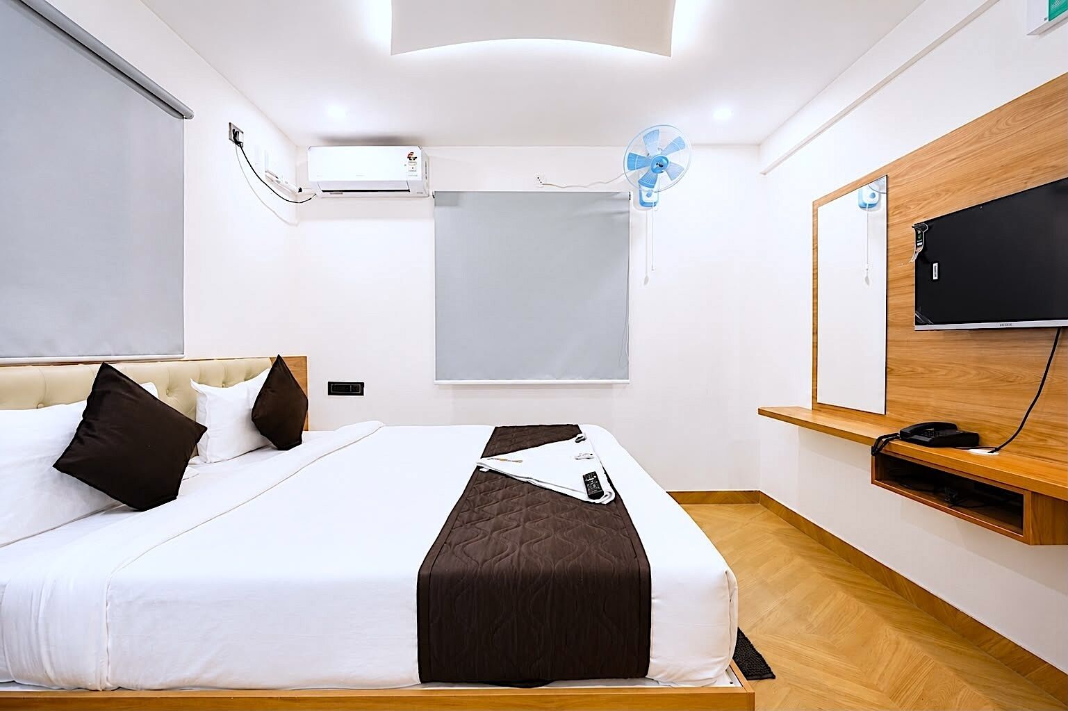 Moderni hotellihuone, jossa on sänky, ilmastointilaite, ikkuna, televisio ja puinen hylly.