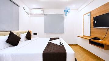 Moderni hotellihuone, jossa on sänky, ilmastointilaite, ikkuna, televisio ja puinen hylly.
